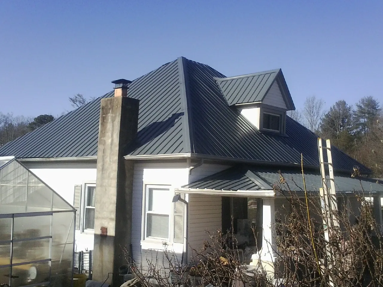 Dark blue standing seam metal roof on a white farmhouse with dormer — Slate & Tile Roof Repair by Roofing Brothers in Island Lake