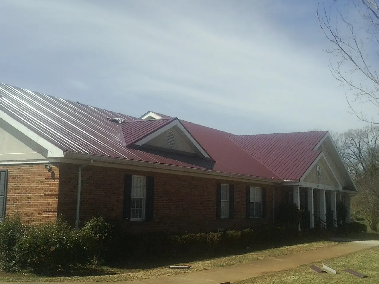 Red metal roof with gabled entries on a long brick building, from a Hail Damage Roof Repair job in Island Lake