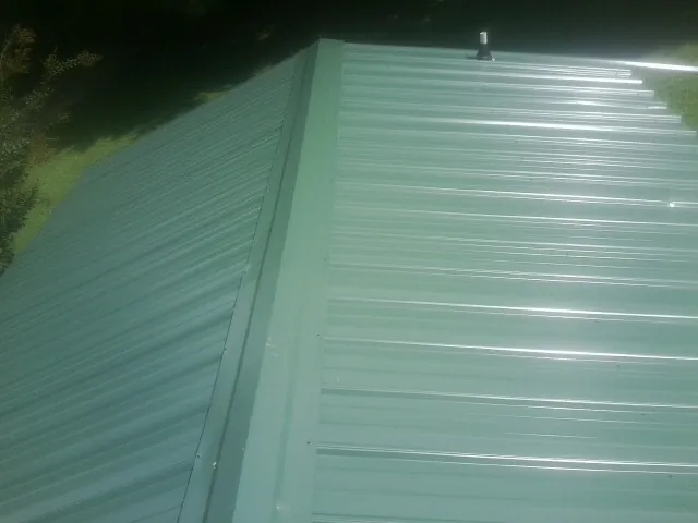 New green metal panels meeting at the ridge of a roof — Flat Roof Repair work by our crew in Island Lake
