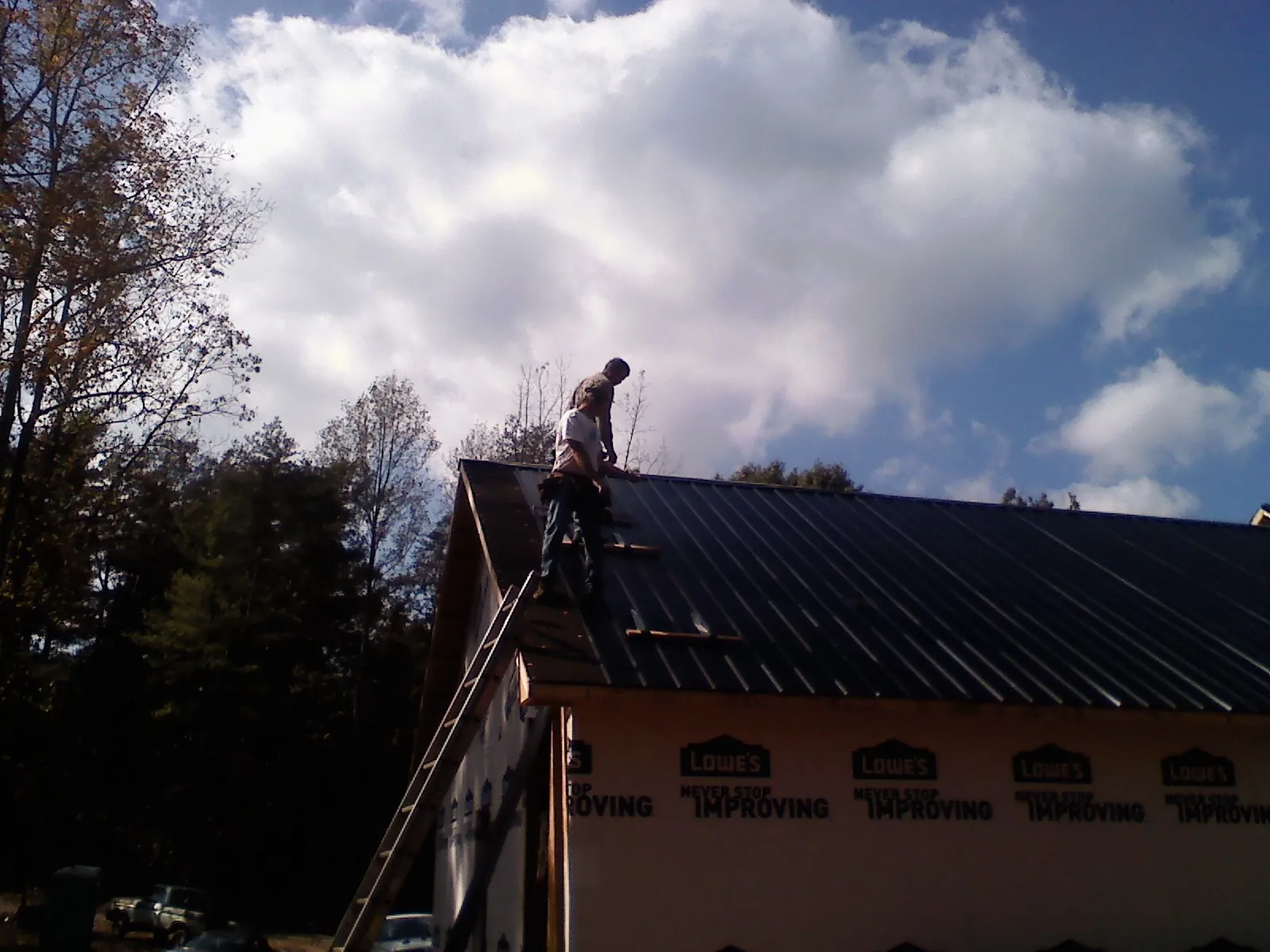 Roofer fastening dark metal panels high against a cloudy sky, from a Roof Inspection job in Island Lake