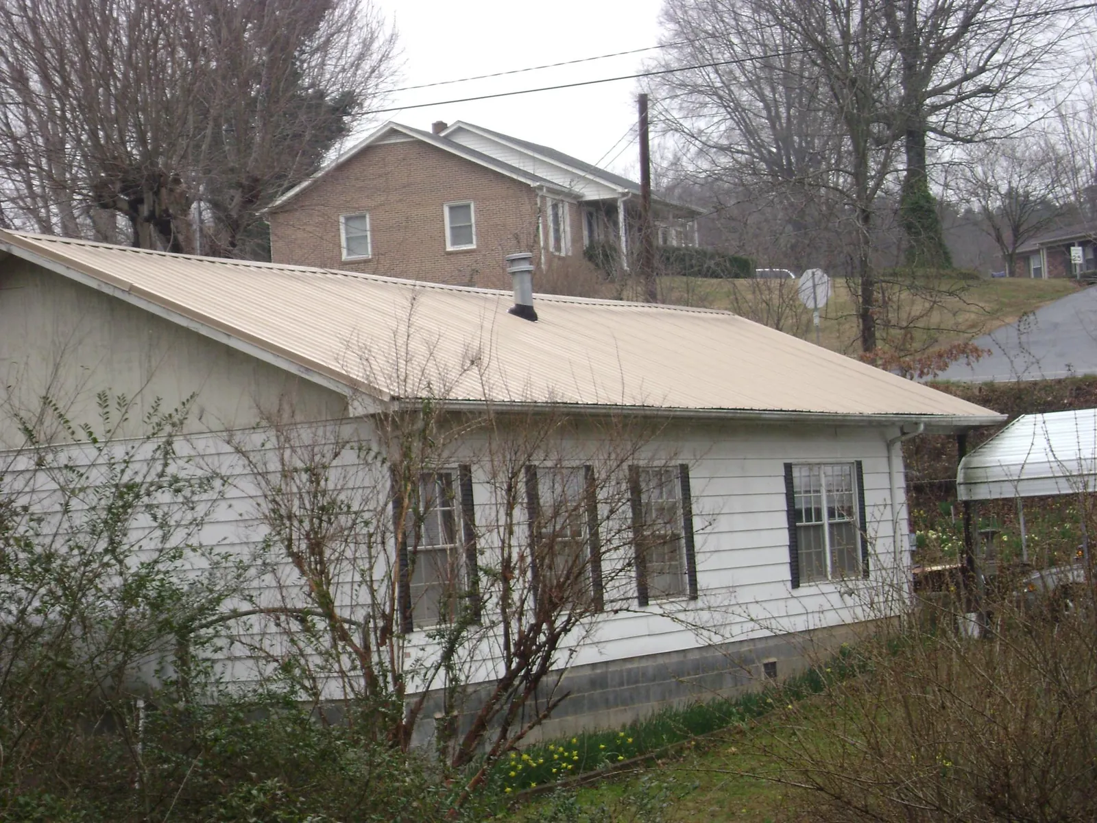 Tan metal roof on a white sided house set into a hillside — Commercial Roofing by Roofing Brothers in Island Lake