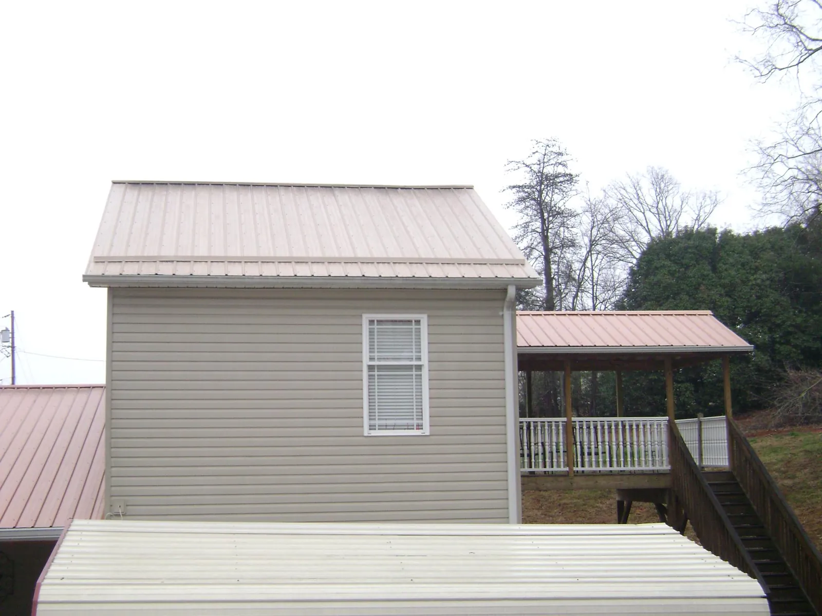 Tan metal roofs on a two story addition and attached porch, from a Roof Replacement job in Island Lake